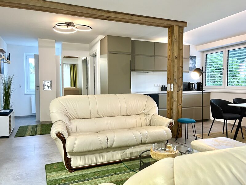 Wohnbereich mit cremefarbenem Sofa, Holzbalken als Raumteiler und moderner Beleuchtung