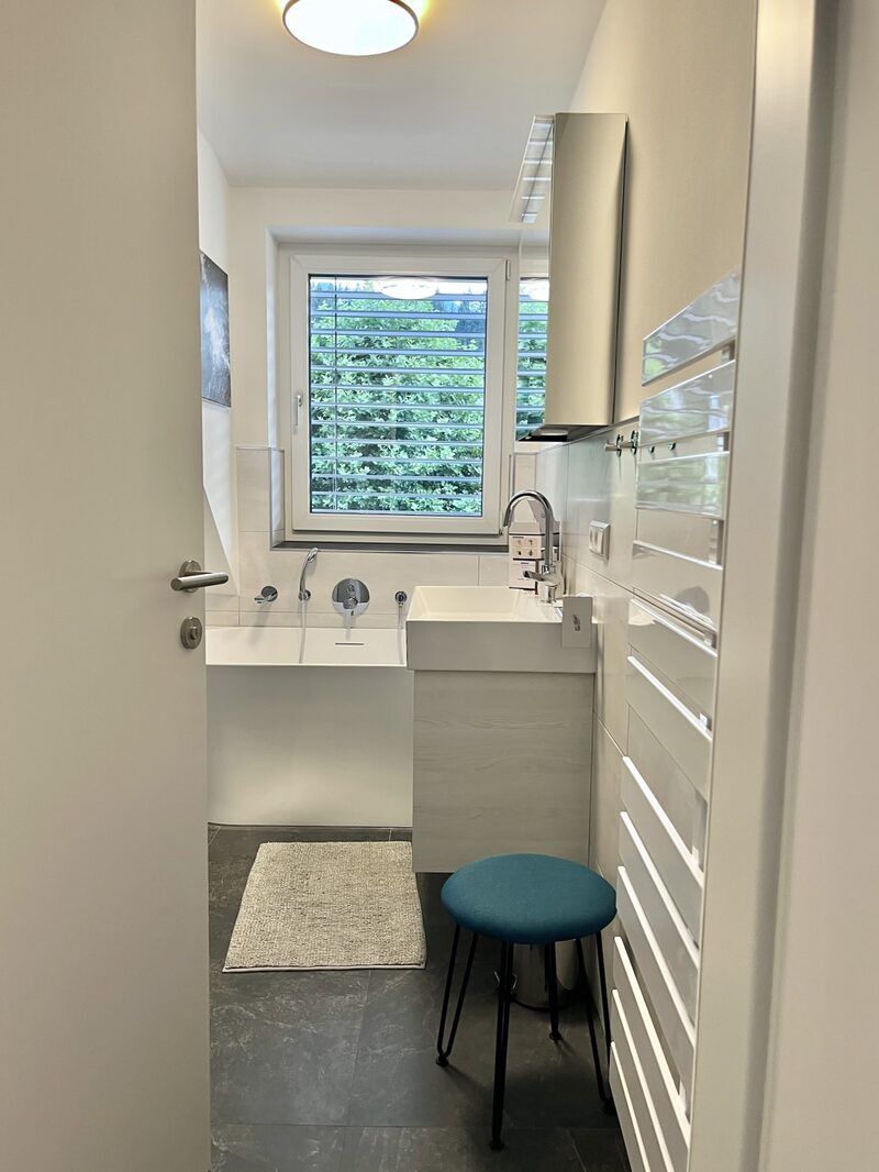 Badezimmerdetail mit Hocker, großem Waschbecken und Handtuchheizkörper